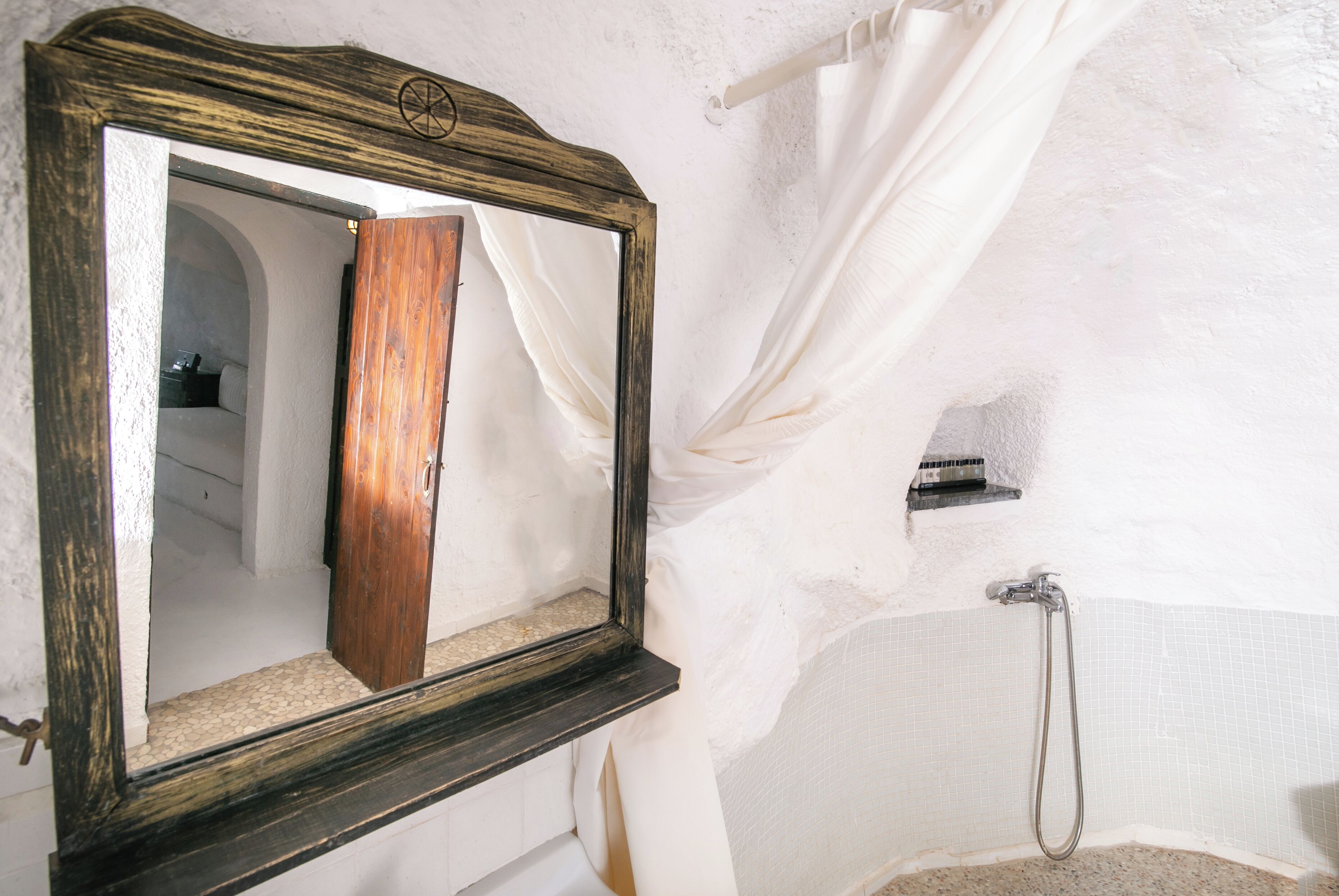 Un baño con espejo de marco de madera, ducha y pared con azulejos blancos.