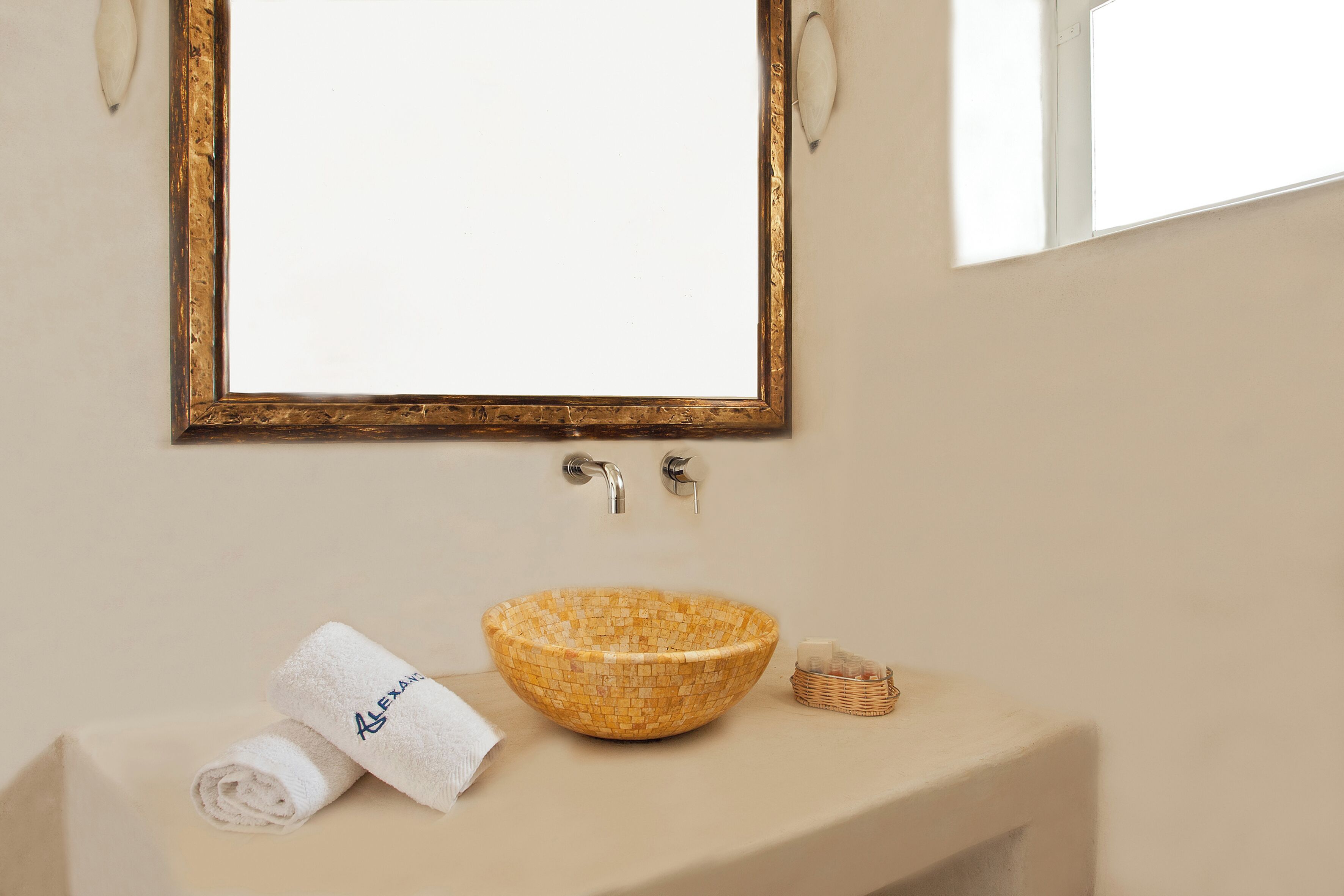 Un baño con un lavabo de mosaico, una toalla con un nombre y una cesta pequeña.