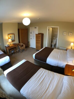 Habitación de hotel con dos camas, un escritorio con lámpara, un armario y un baño visible a través de una puerta abierta.