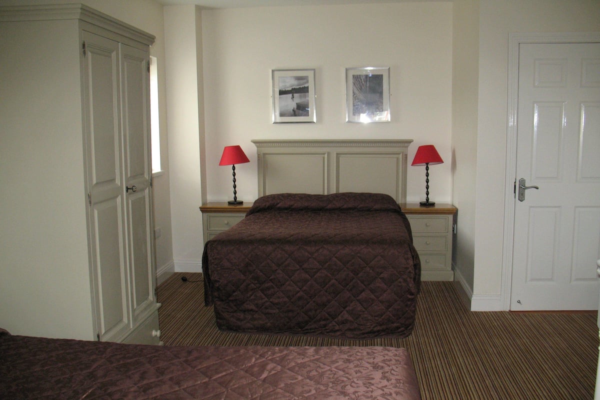 A hotel room with a queen-sized bed, a smaller bed, two bedside tables with lamps, a dresser, and a door.