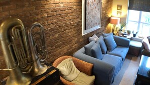 Una sala acogedora con pared de ladrillo, un sofá, una silla de mimbre e instrumentos de viento de latón.