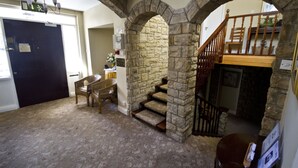 Una habitación con un arco de piedra que conduce a una escalera, una silla de madera y una pequeña mesa con un florero.