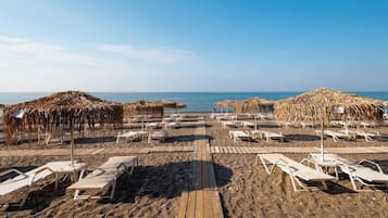 A beach with sun loungers and thatched umbrellas, a wooden walkway, and the sea in the background.