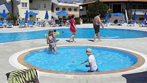 Un espace piscine avec des chaises longues et des parasols, entouré de bâtiments.