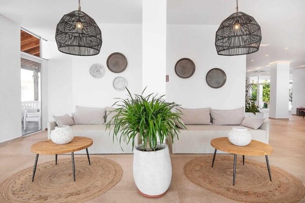 A modern living room with a sofa, two side tables, a large potted plant, and decorative wall plates.