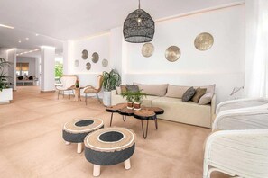 Un salon moderne avec un canapé, deux poufs ronds, une table basse et un luminaire suspendu.