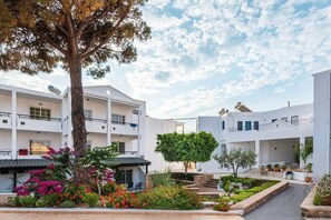 A multi-story building with balconies, surrounded by landscaped gardens and trees.