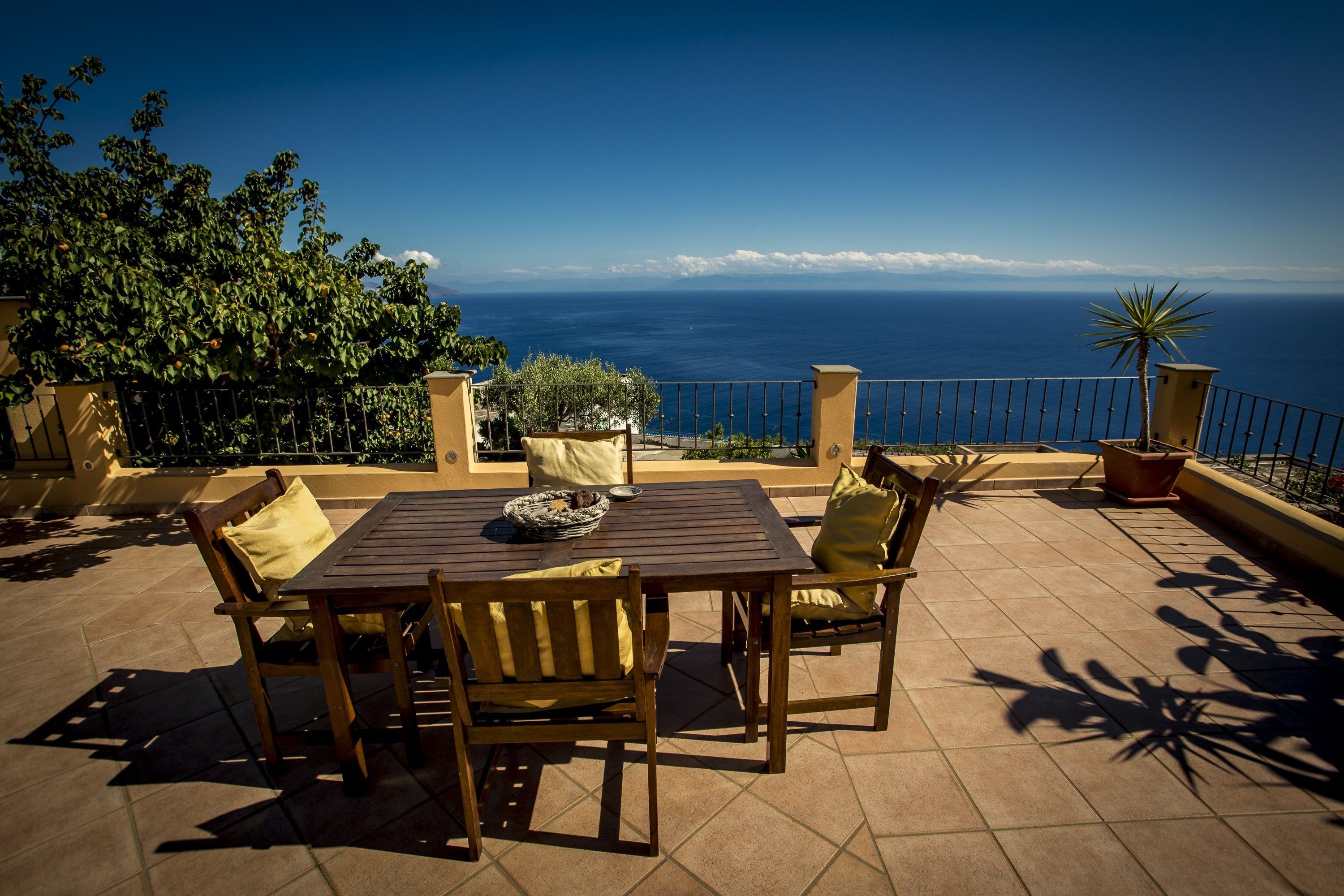 A terrace with a table and chairs, a view of the ocean, and potted plants.