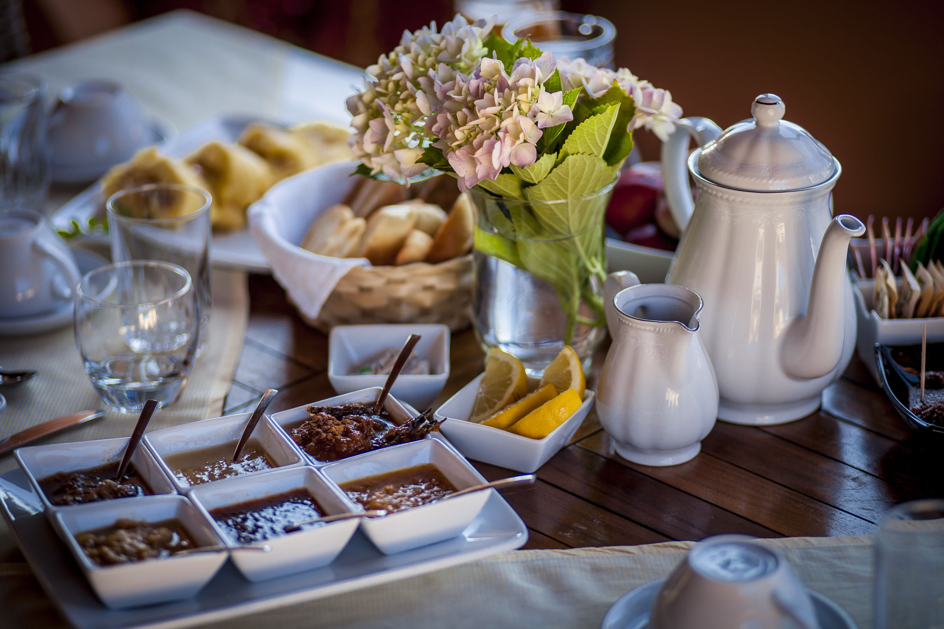 A breakfast setting with various food items, a teapot, and a vase of flowers.