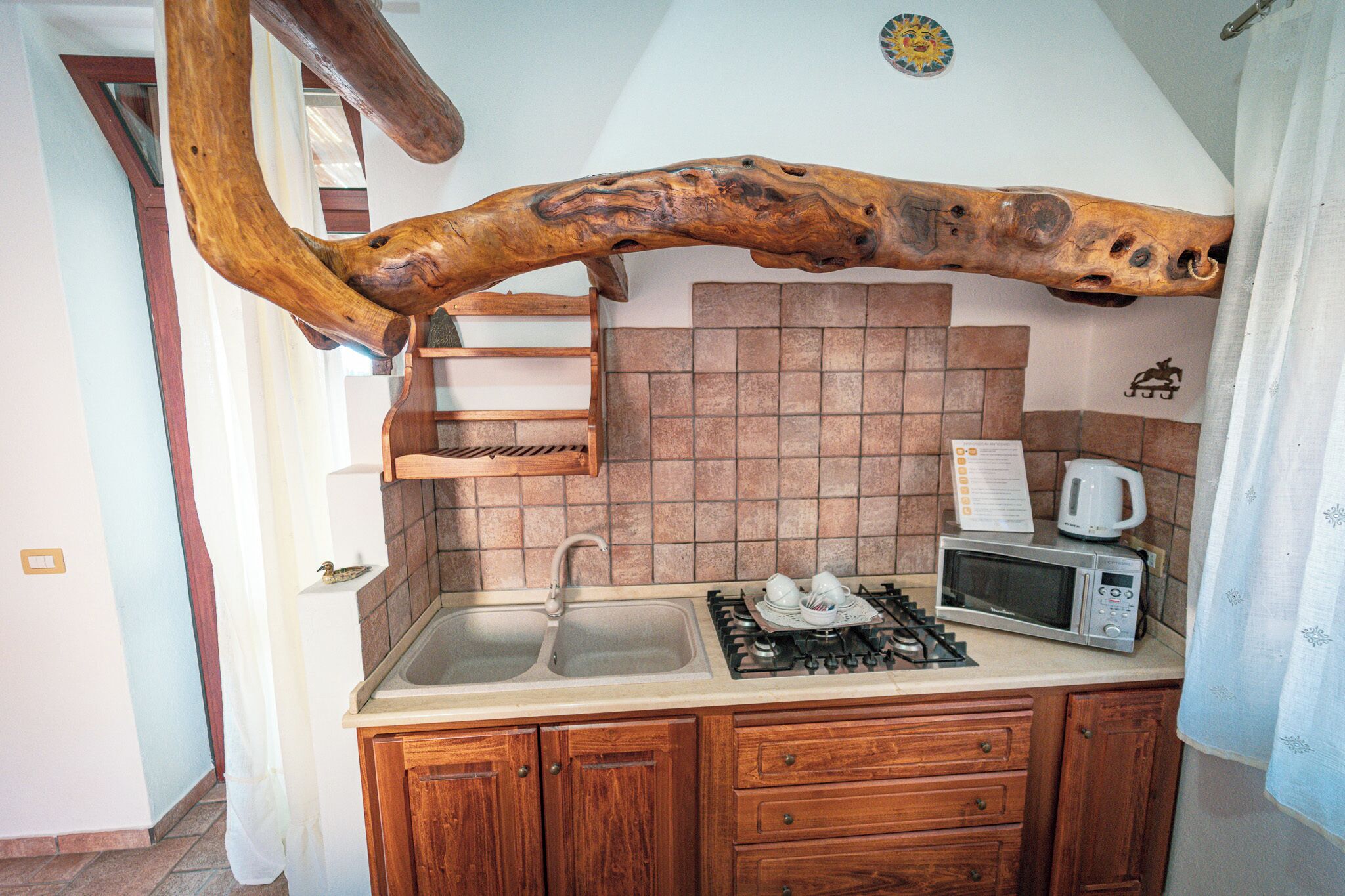 A kitchen with a wooden beam ceiling, a sink, a stove, a microwave, and wooden cabinets.