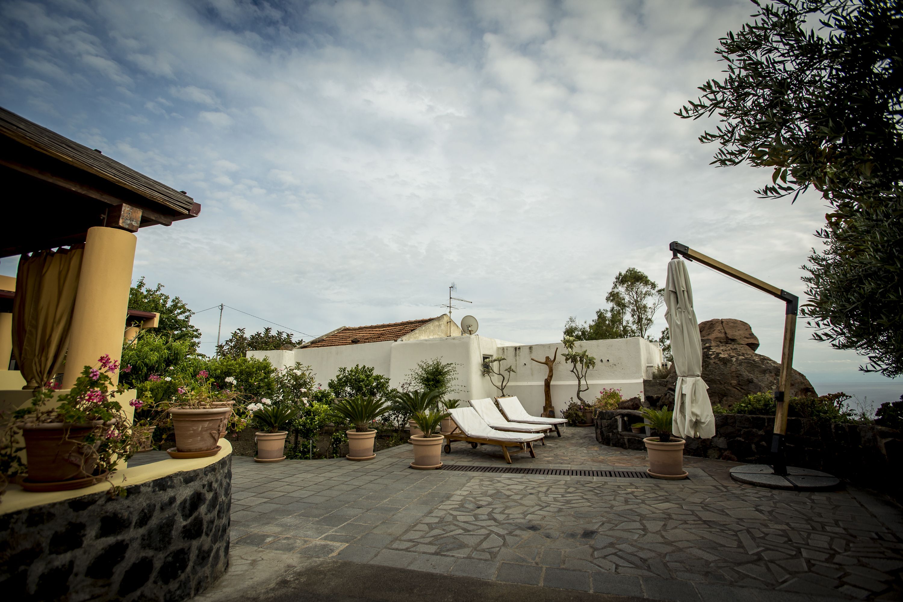 A patio with lounge chairs, potted plants, and a stone wall.