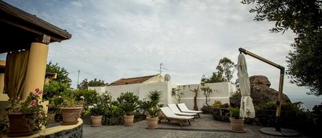 A patio with lounge chairs, potted plants, and a stone wall.