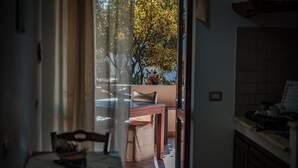 A view from a room into a dining area with a table and chairs, a window with curtains, and a view of trees outside. - Al Belvedere Salina (Leni)