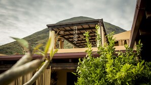 A building with a covered patio area, a mountain in the background, and lush greenery in the foreground. - Al Belvedere Salina (Leni)