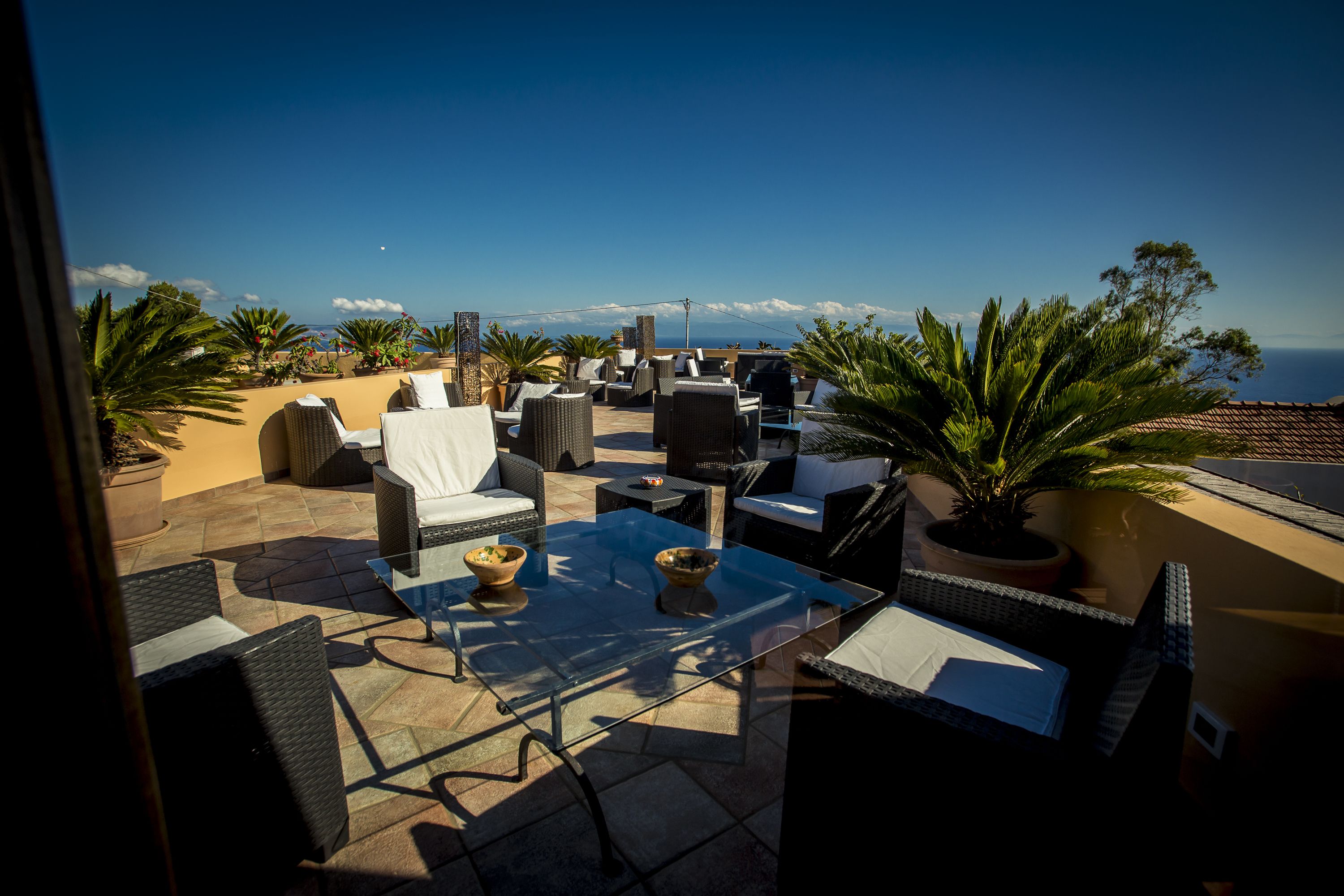 Una terraza en la azotea con mobiliario exterior, una mesa de vidrio y plantas en macetas.