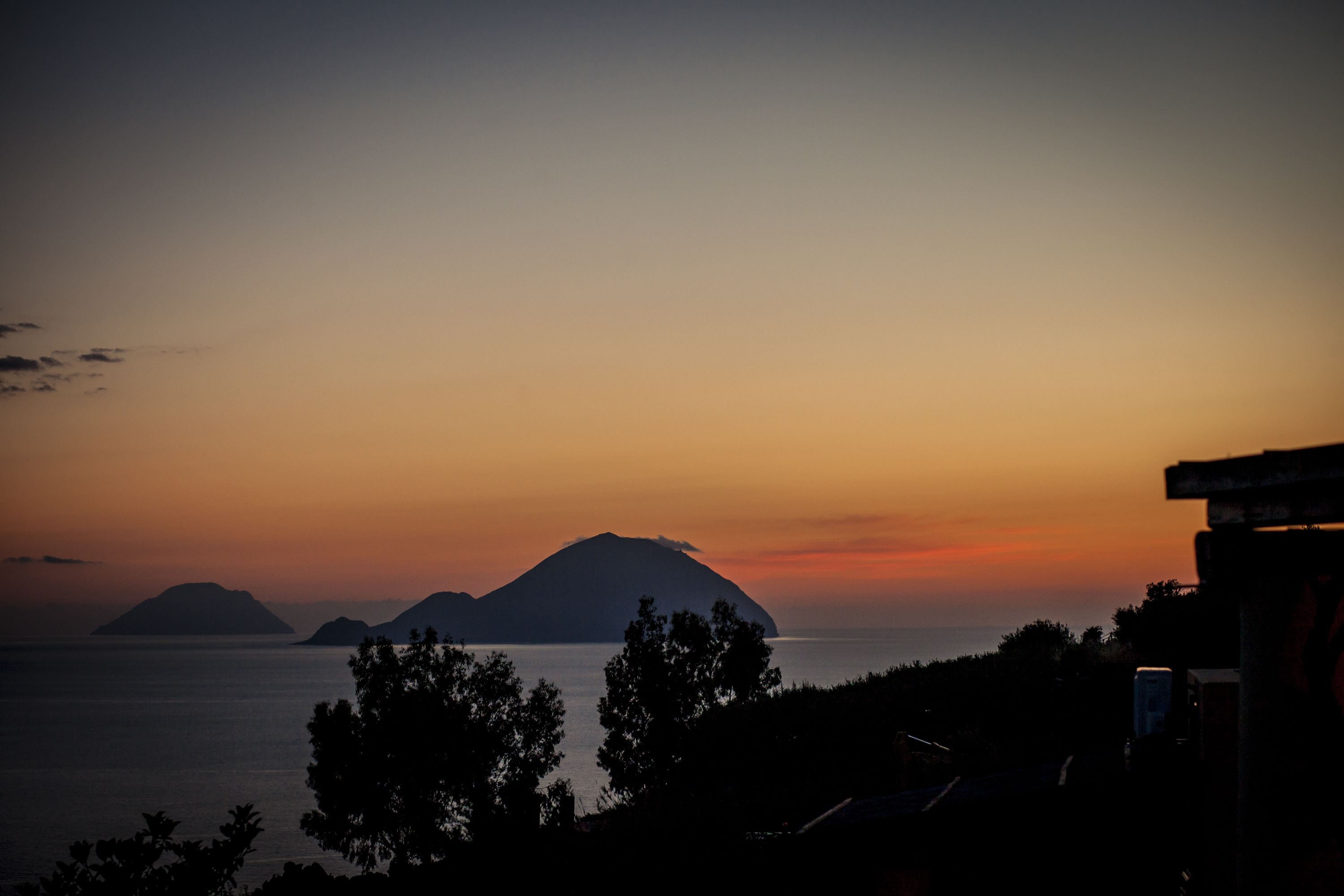 A coastal sunset view with silhouettes of mountains and trees.