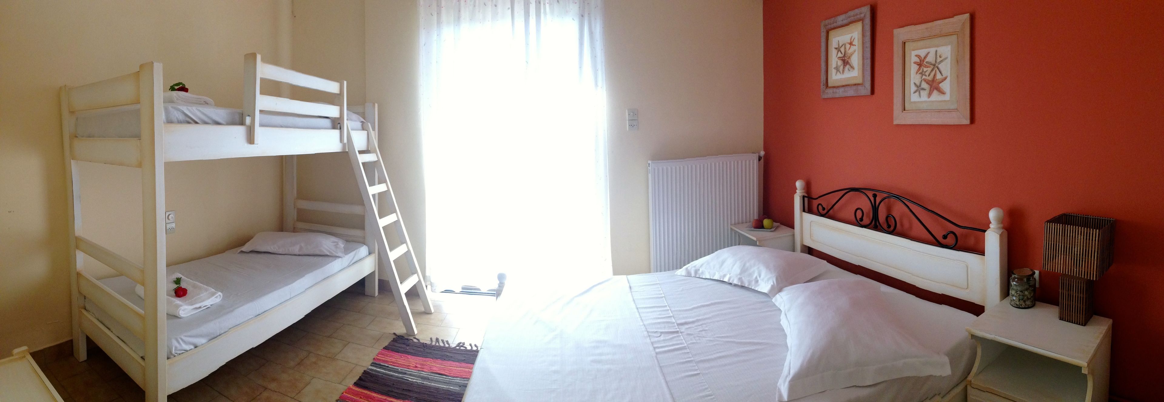 Una habitació amb dos llits superposats, un llit individual, un radiador, una tauleta de nit amb una làmpada i quadres a la paret.