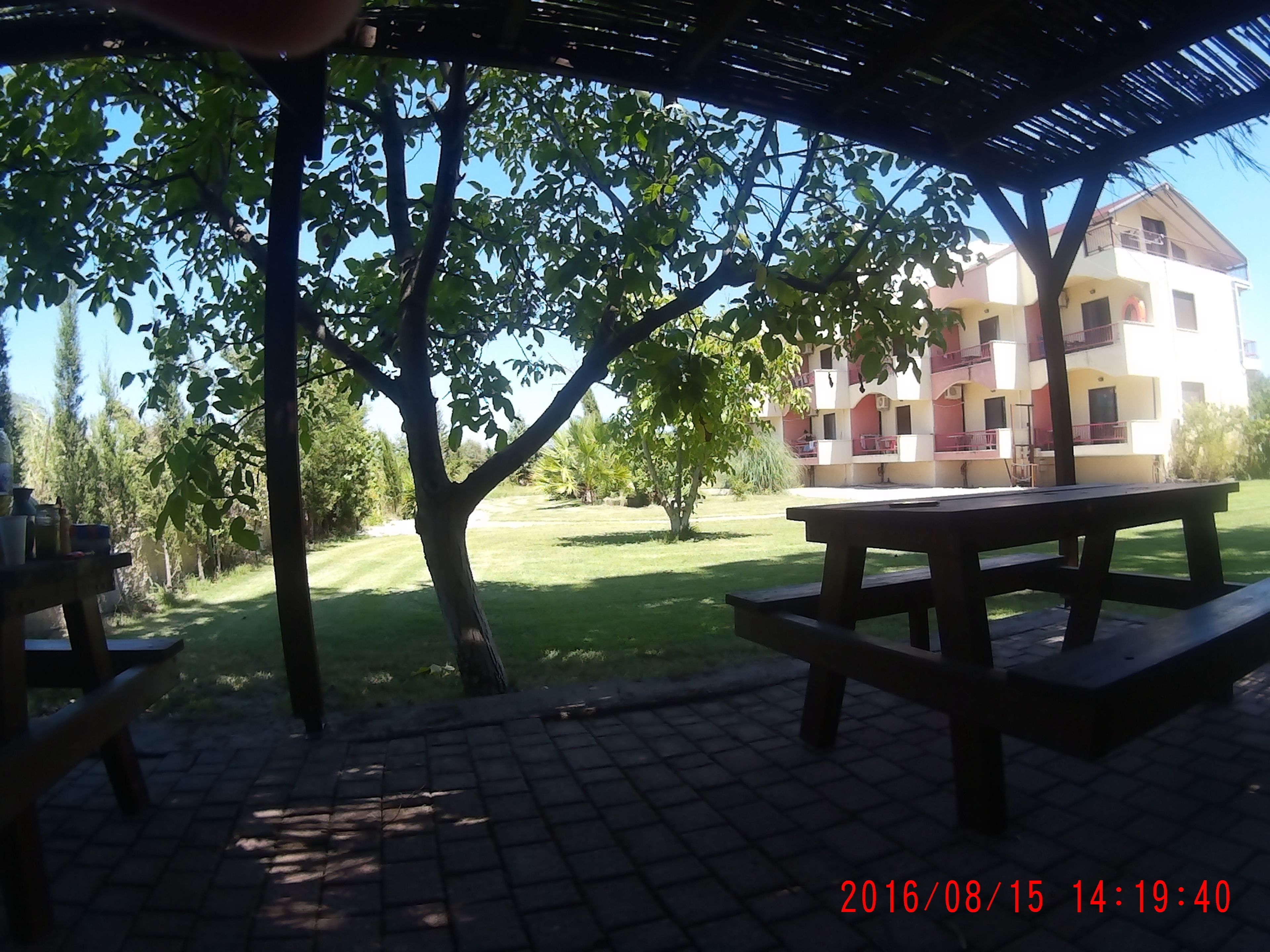A covered outdoor area with picnic tables and a building in the background.