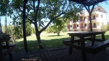 A covered outdoor area with picnic tables and a building in the background.