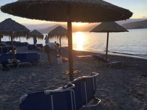 Una playa con sombrillas de paja, sillas de descanso y vistas al atardecer.