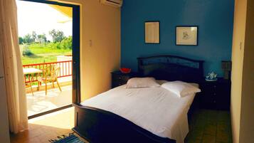 Un dormitorio con cama, mesita de noche, silla y vistas a un balcón.