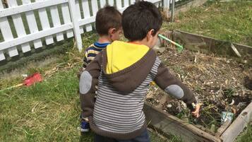 Dos niños jugando en un jardín con una cerca blanca de piquetes al fondo.