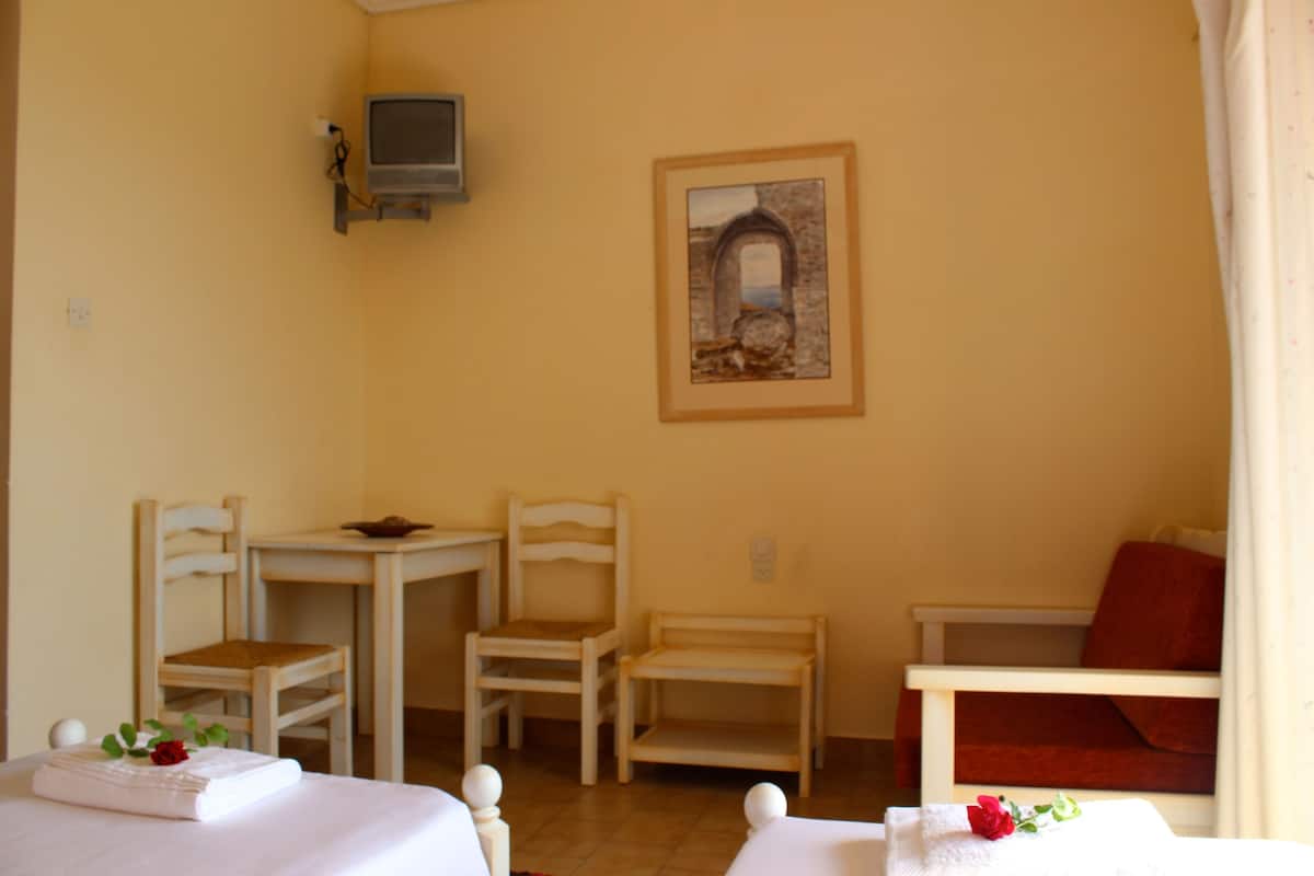 A room with two beds, a small table, two chairs, a TV, and a painting on the wall.