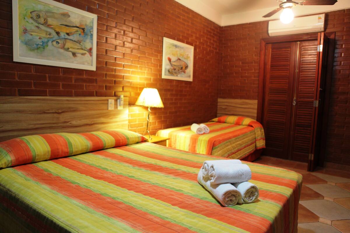 A hotel room with two beds, a brick wall, a ceiling fan, and a door.