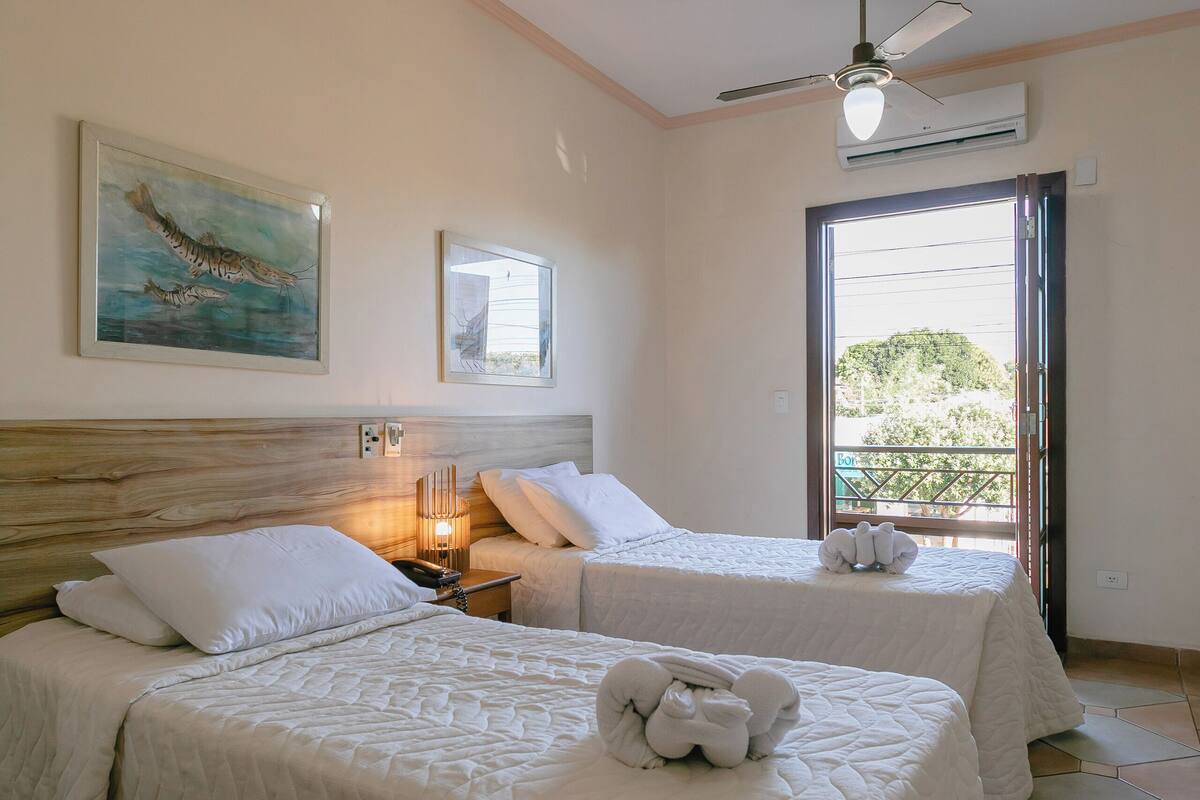A hotel room with two beds, a ceiling fan, artwork on the walls, and a view through the door.