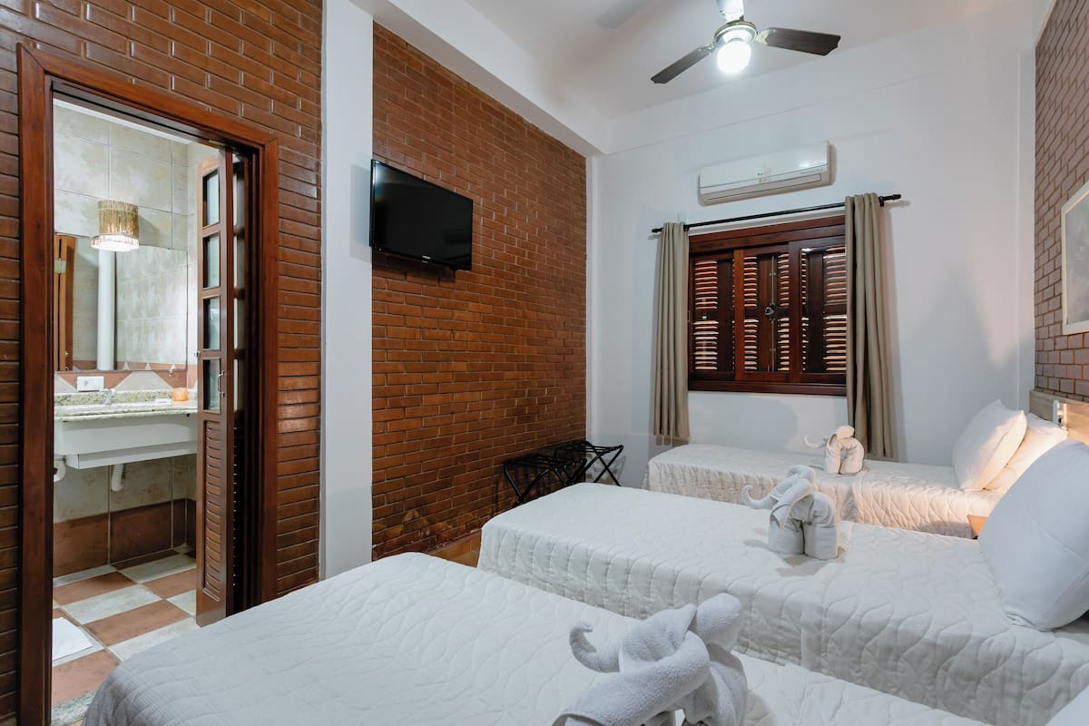 A hotel room with two beds, a television, an air conditioning unit, and a brick wall.