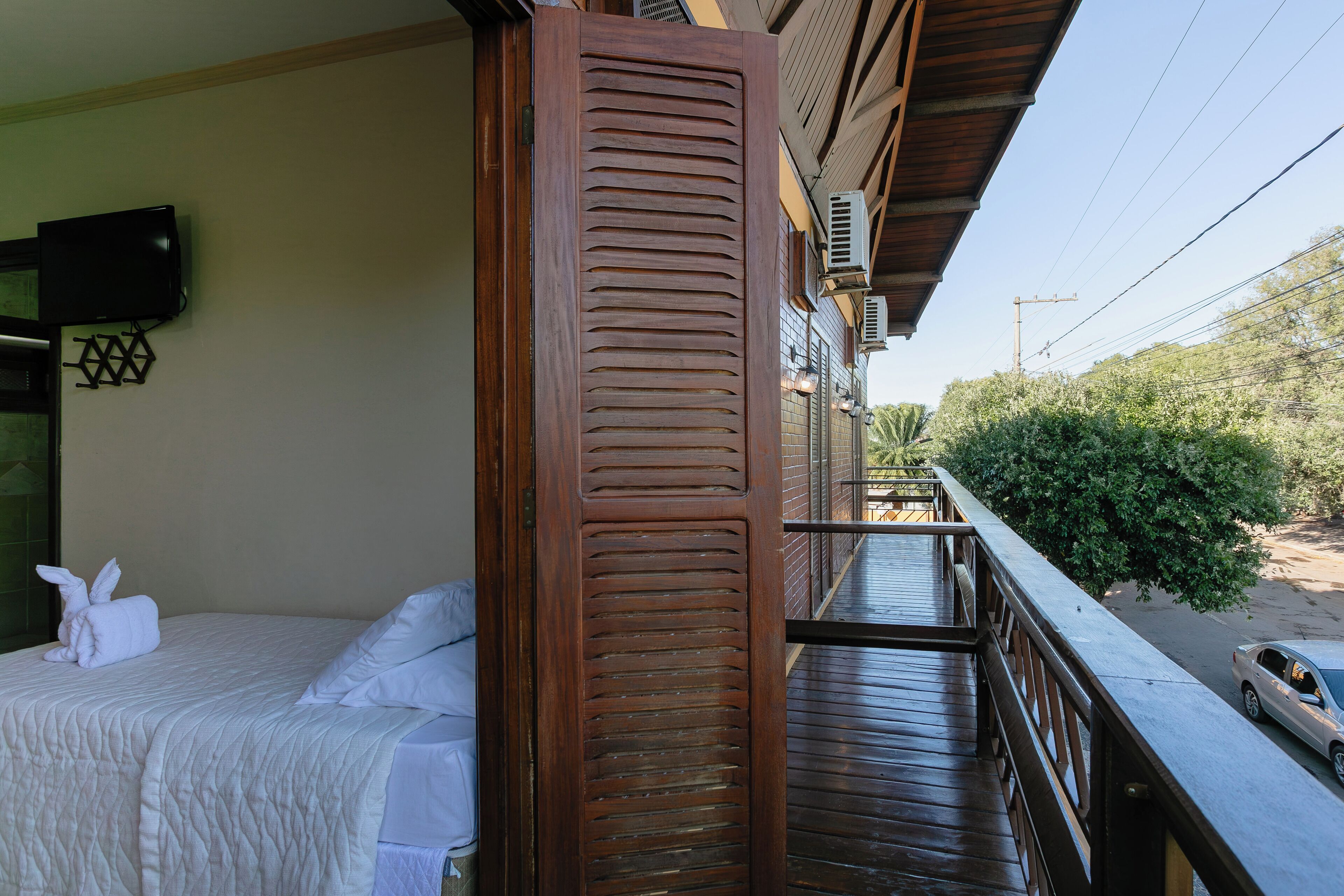 Habitación de hotel con cama, barandilla de madera en el balcón y vista a la calle y zonas verdes.