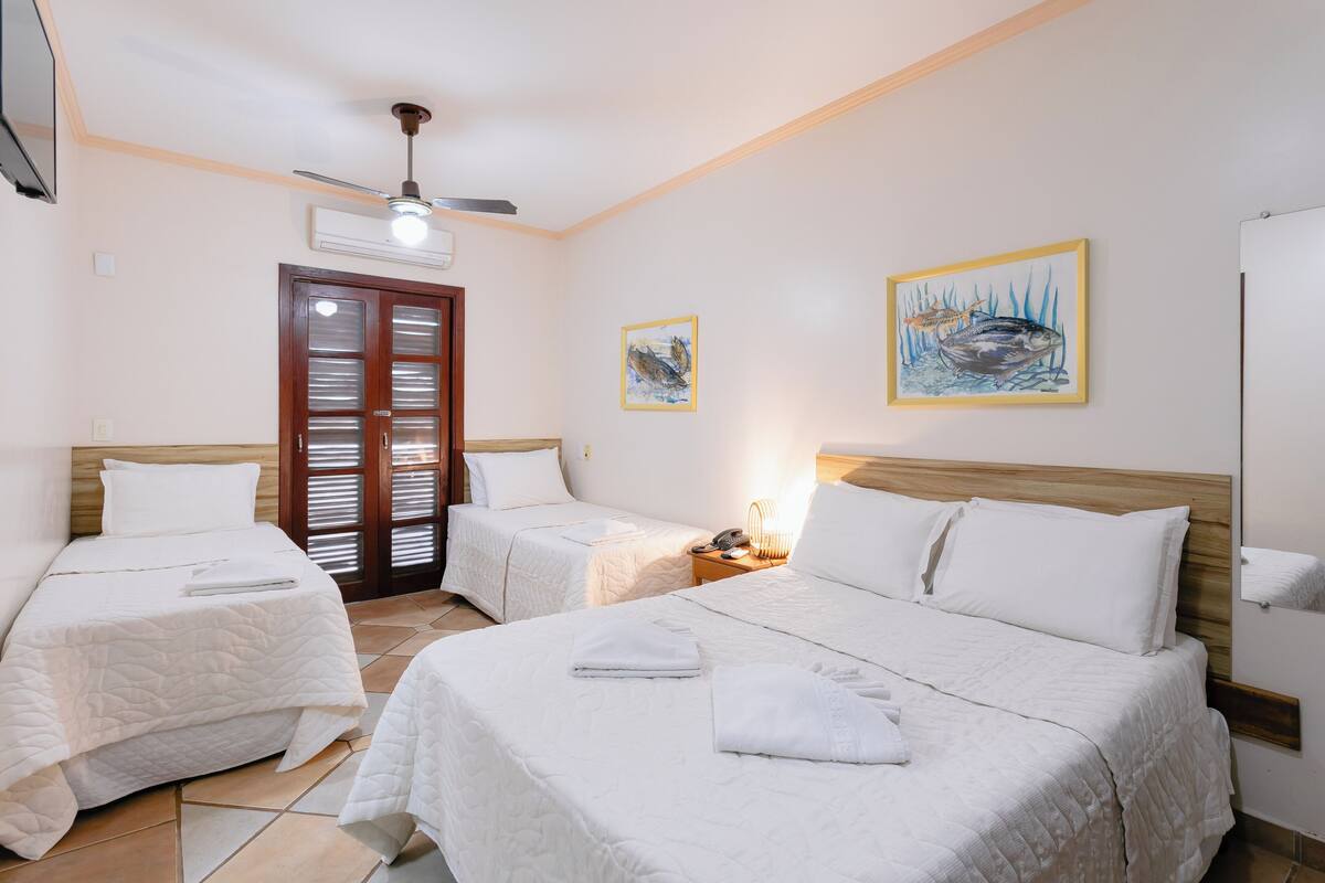 A hotel room with two beds, a ceiling fan, and artwork on the walls.