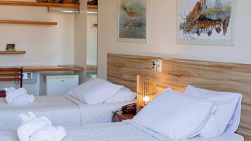 A hotel room with two beds, white bedding, a wooden headboard, a bedside table with a lamp, and artwork on the walls.