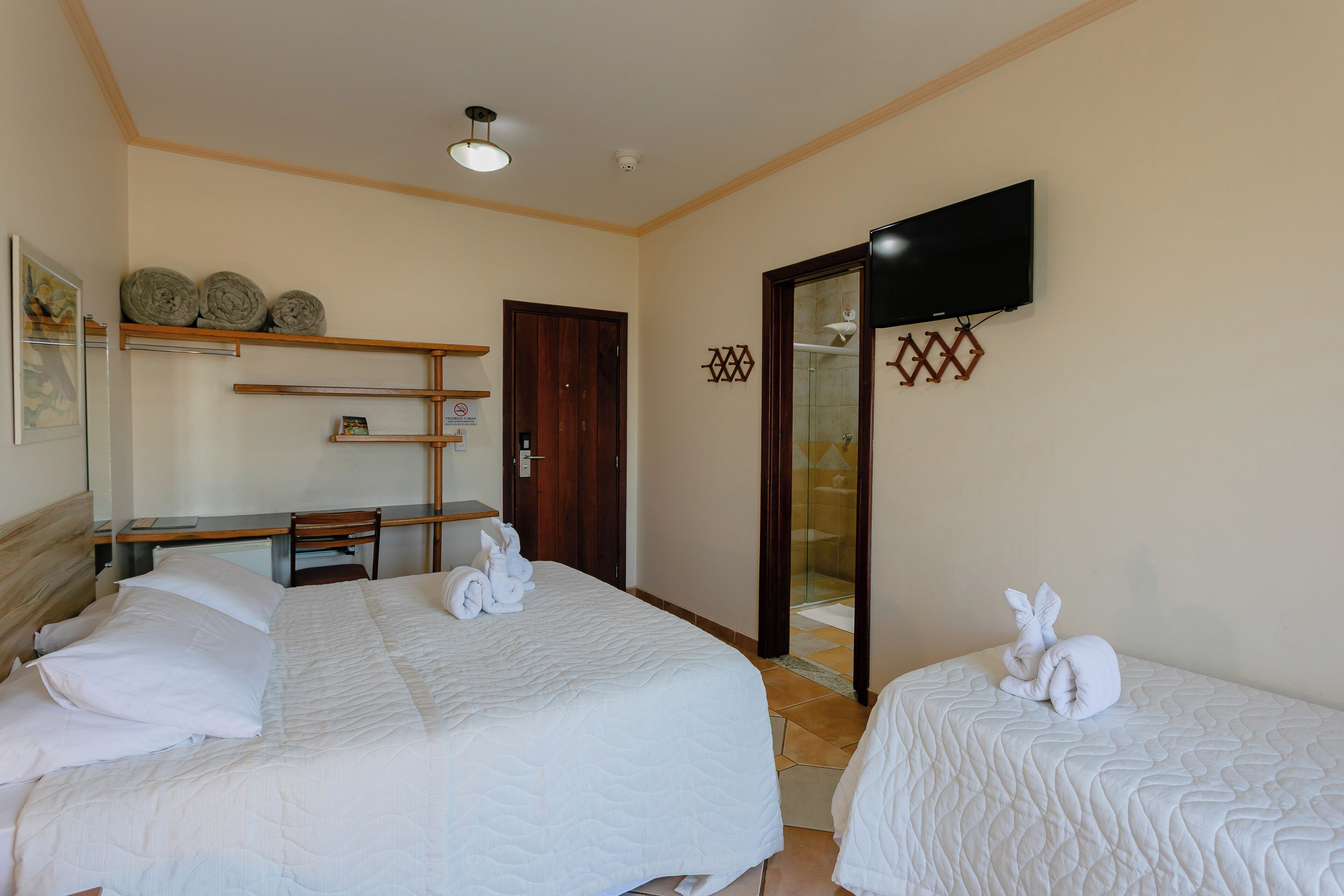 Habitación de hotel con dos camas, un escritorio, una silla, un televisor y una puerta que da a un baño.