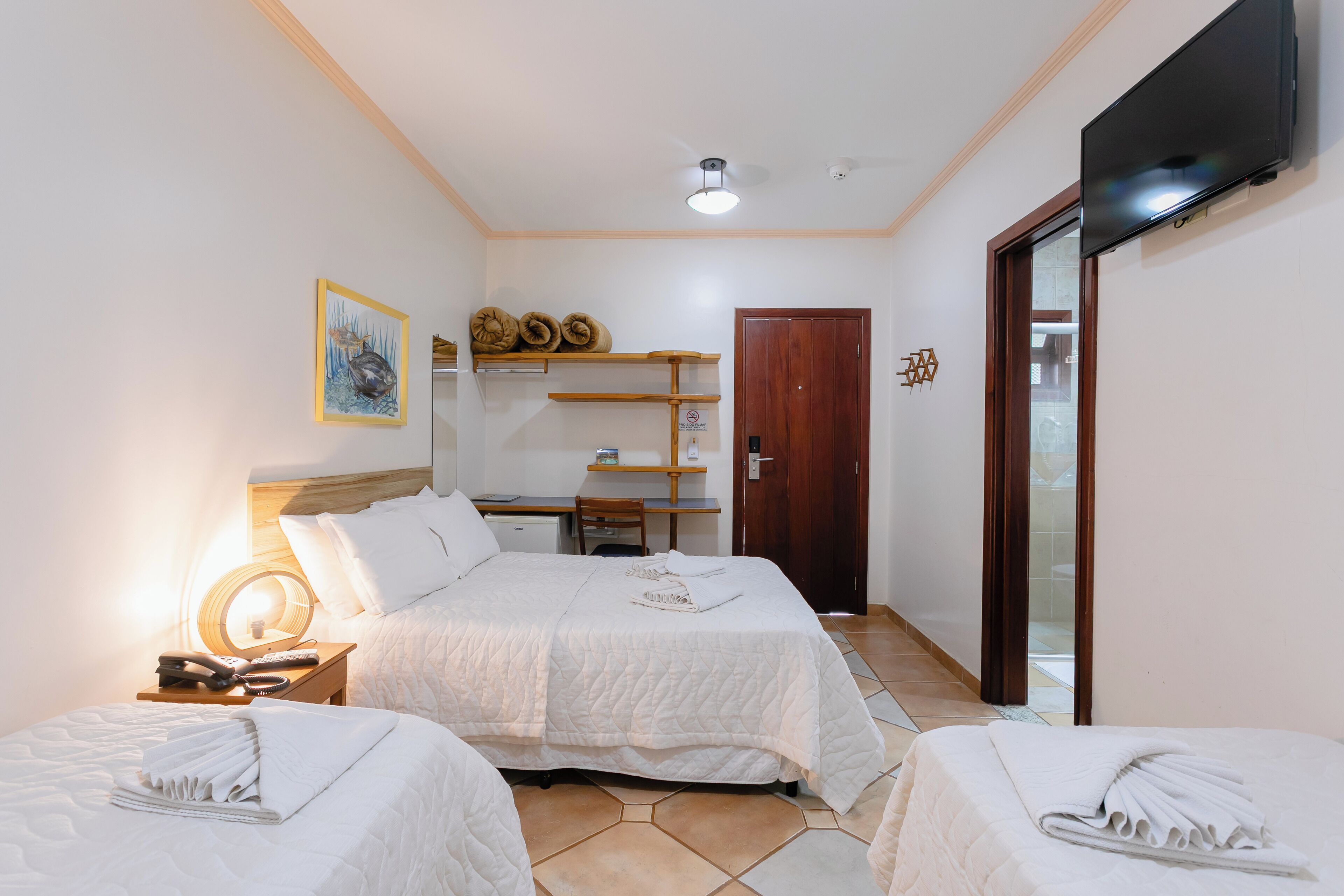 Camera d'albergo con due letti, una scrivania, una sedia, una televisione e un'uscita che dà su un balcone.