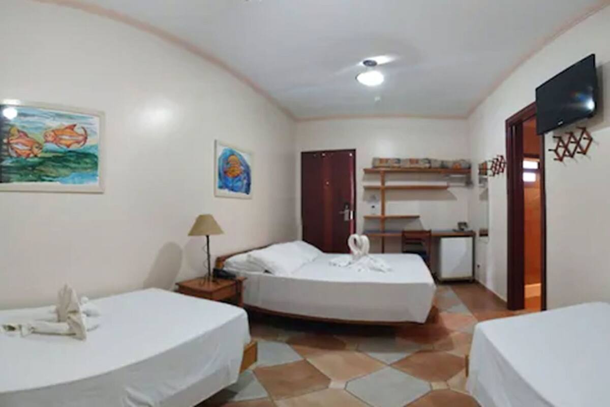 A hotel room with two beds, a desk, a chair, a TV, and artwork on the walls.