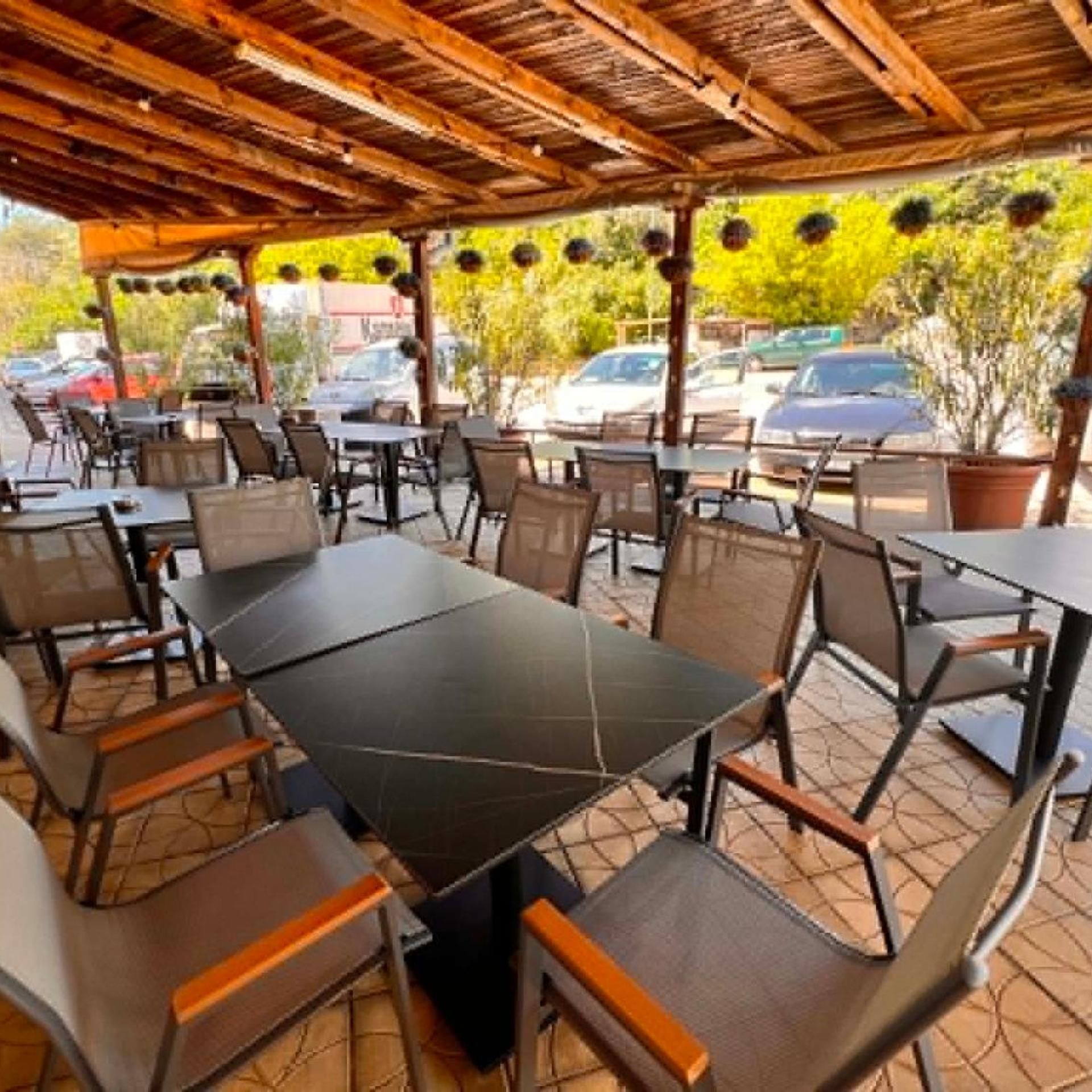 An outdoor patio area with tables and chairs, a wooden ceiling, and hanging plants.