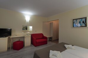 A hotel room with a bed, a red chair, a desk with a TV, and a painting on the wall. - Detelina (Varna)
