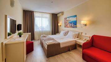 A hotel room with a bed, a desk, a red sofa, a painting, and a window with curtains.
