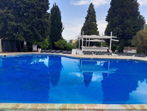A swimming pool with lounge chairs and a covered seating area, surrounded by trees. - Detelina (Varna)