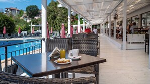 An outdoor seating area with a pool view, wicker furniture, and a table with a drink and a plate of food. - Detelina (Varna)