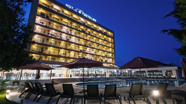 A hotel with multiple balconies, a pool area with lounge chairs and umbrellas, and a well-lit exterior. - Detelina (Varna)