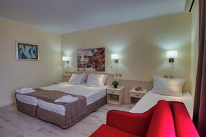 Una habitación de hotel con cama, mesitas de noche, una silla roja y obras de arte en las paredes.