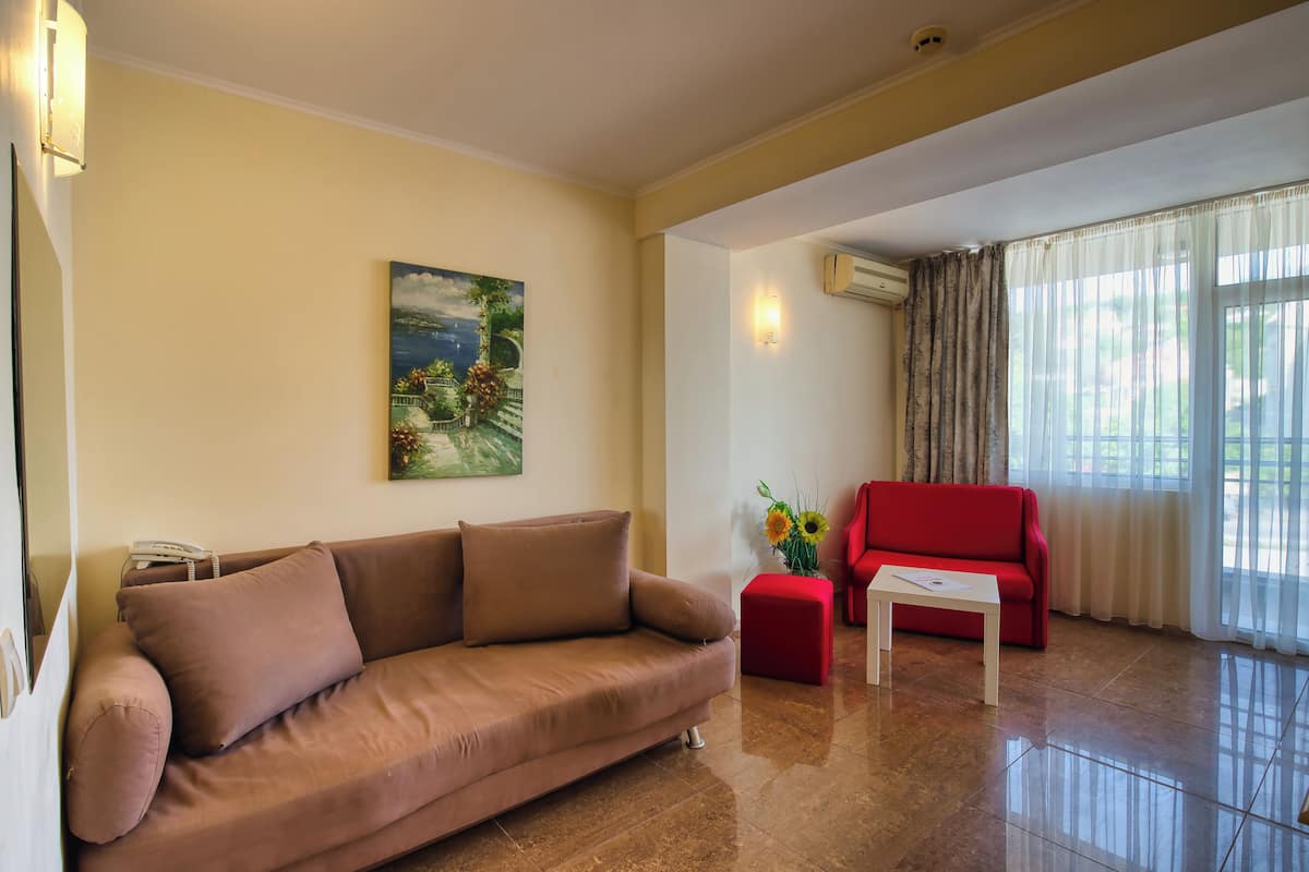 A living room with a sofa, a red armchair, a coffee table, a painting on the wall, and an air conditioning unit.