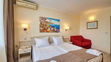 A hotel room with a bed, bedside tables, a red chair, a painting, and a wall-mounted lamp.