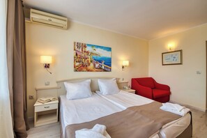 Habitación de hotel con cama, mesitas de noche, una silla roja, un cuadro y una lámpara de pared.