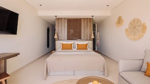 Un dormitorio moderno con una cama grande, un televisor montado en la pared y un rincón de descanso con una silla y una mesa.