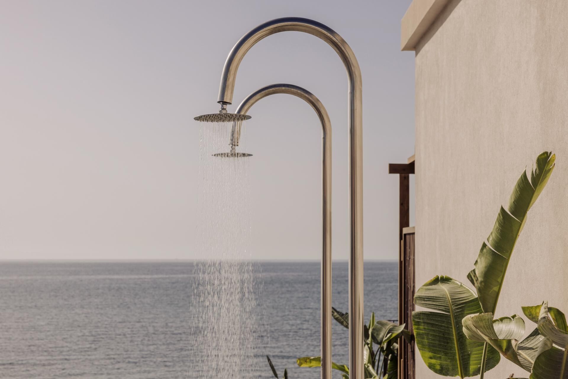 Un pommeau de douche laissant couler l’eau sur un balcon donnant sur la mer.