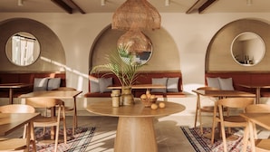 Un restaurante con mesas redondas, sillas de madera y una mesa redonda central con un florero y frutero.