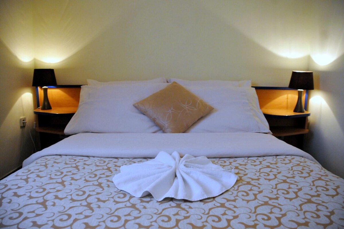 Une chambre d’hôtel avec un lit, deux lampes de chevet et un coussin décoratif.